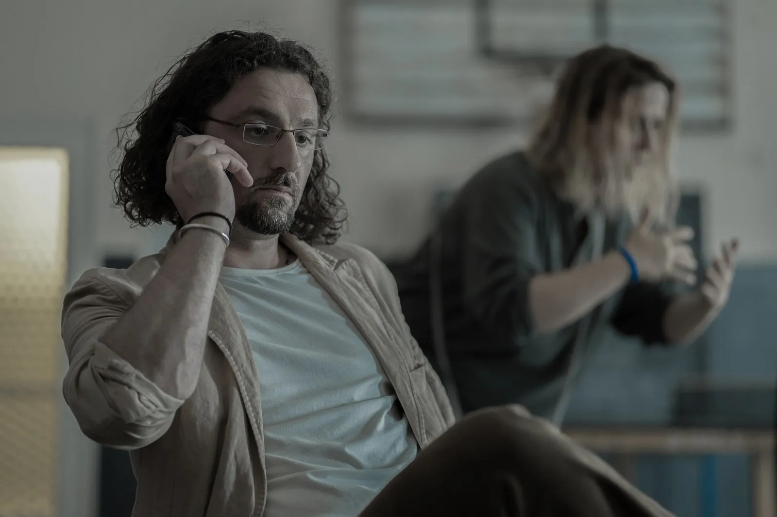 A long haired man staring ahead with an annoyed expression holding a phone to his ear.