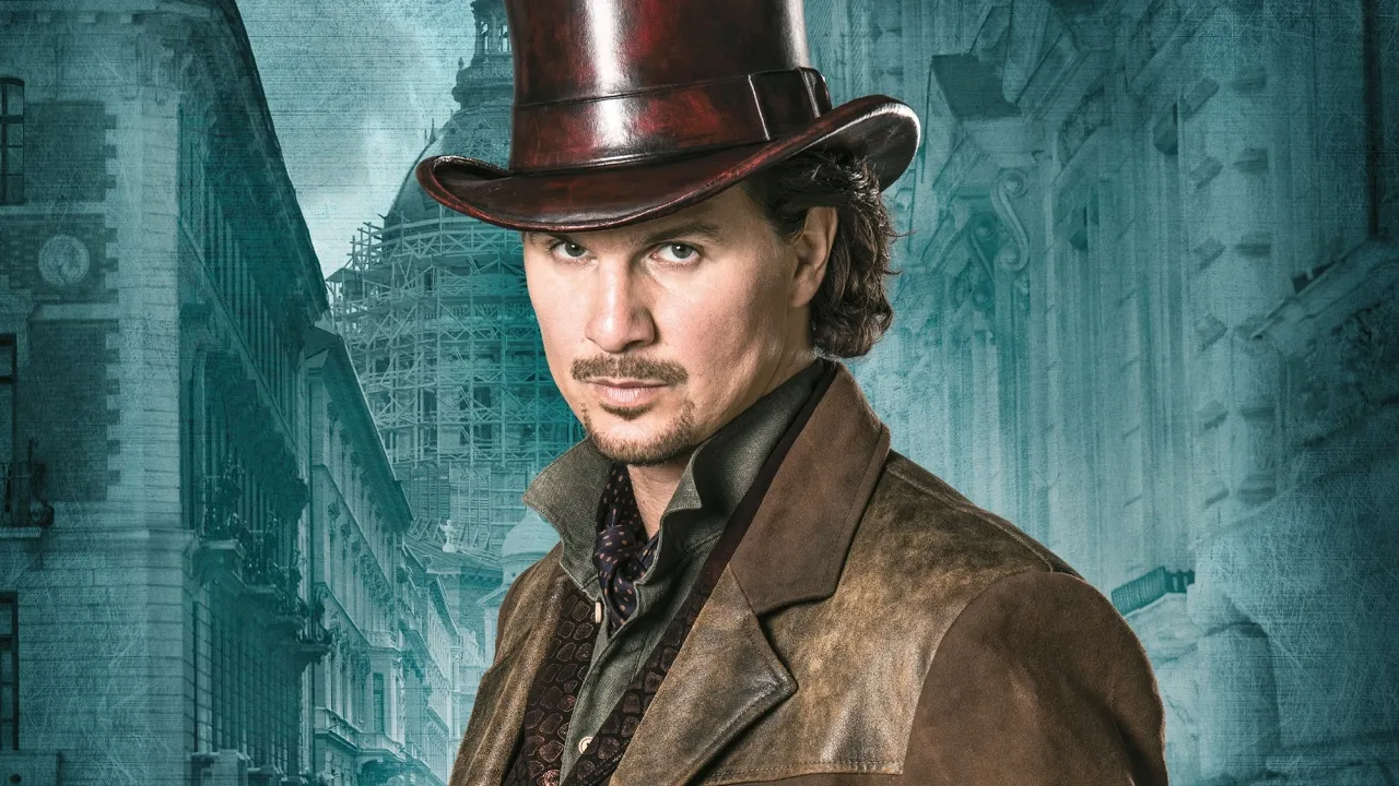 Actor in a brown hat and leather jacket standing in front of a blue building.