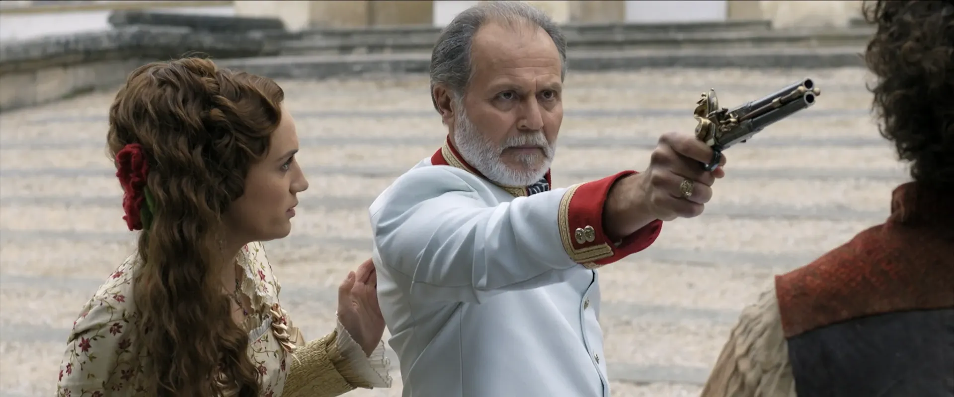 A man in white uniform pointing a gun towards a man only seen from behind, while a lady is looking concerned.