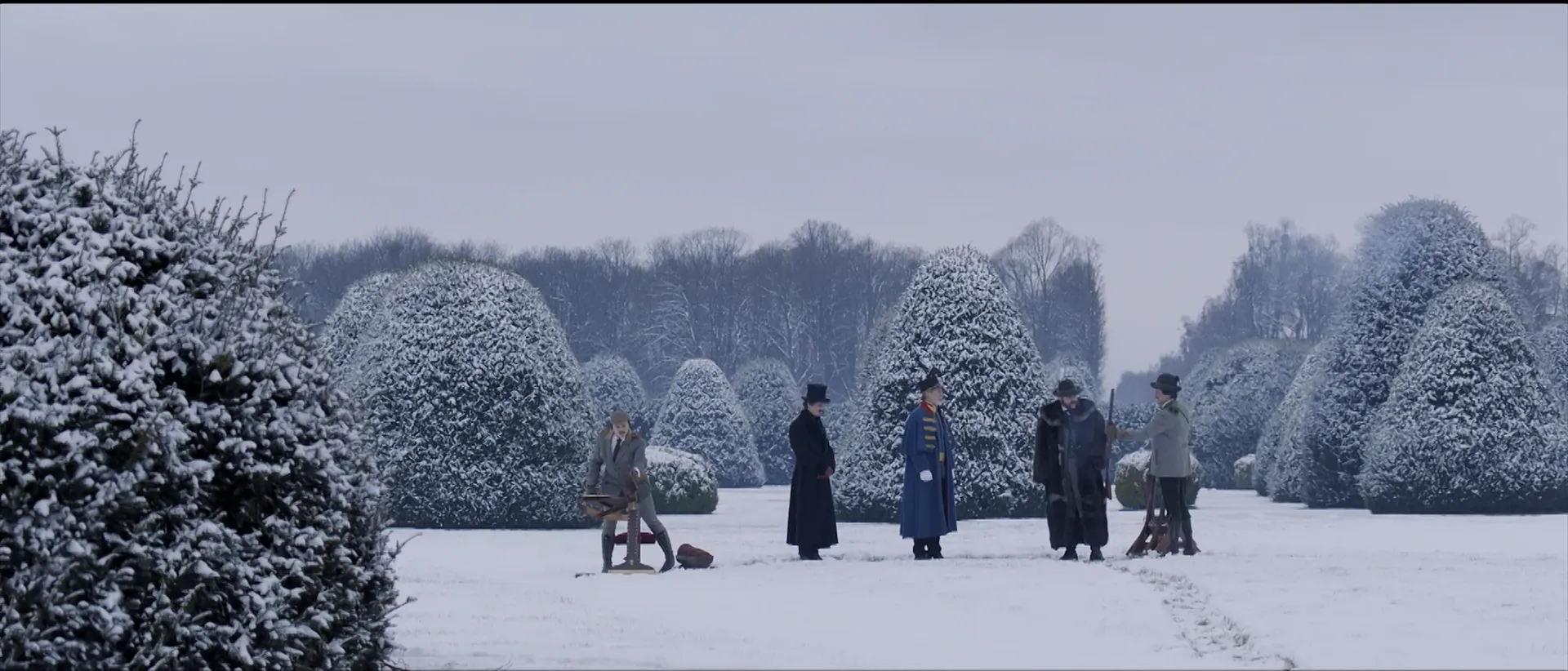 A gathering of five men among a snow covered trimmed bushes with rifles.