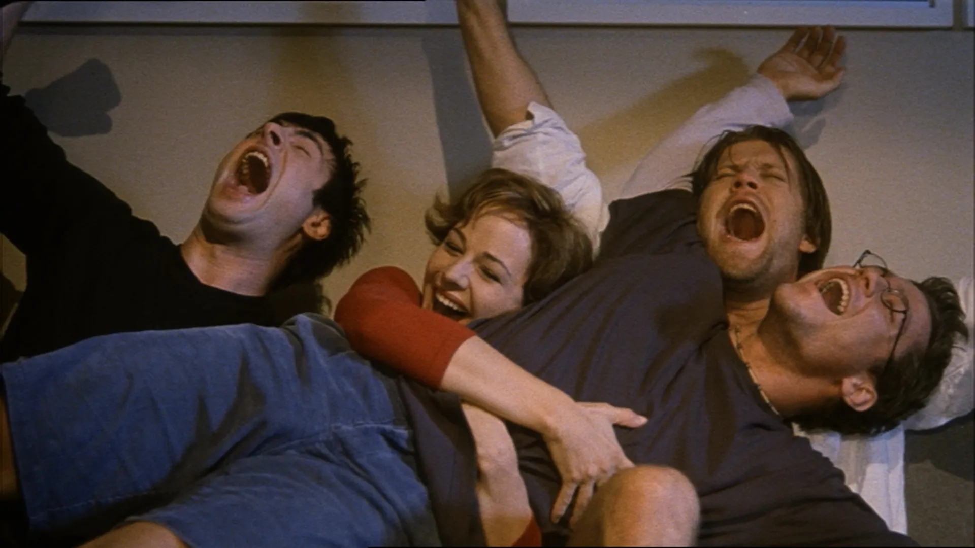 A group of friends lies tangled together, laughing and cheering in a moment of joyful excitement.