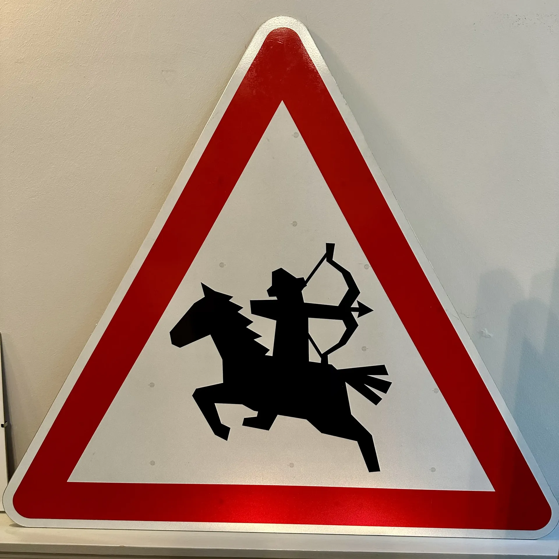 A triangular warning sign with a red border showing a silhouette of a mounted archer riding a horse.