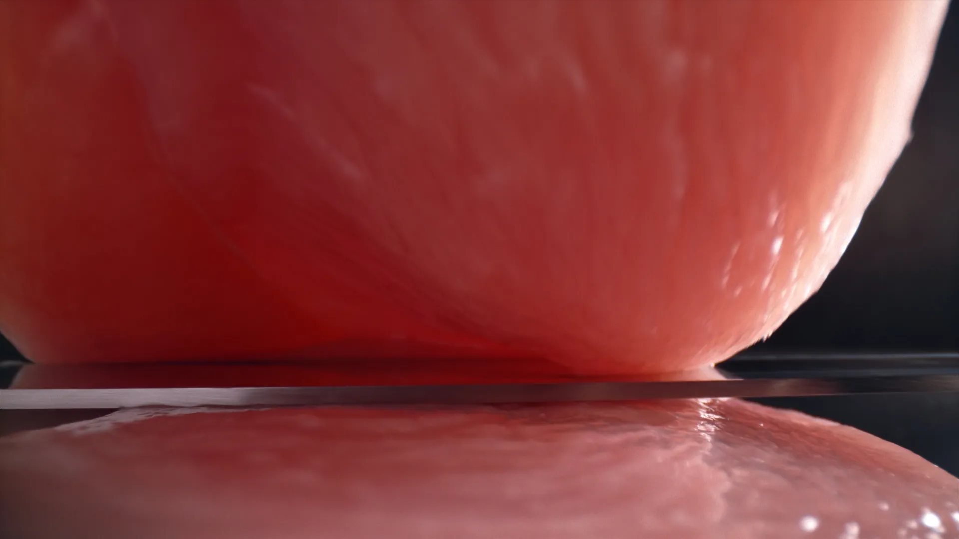 A razor-thin knife slices cleanly through a raw chicken breast in extreme close-up, emphasizing the smooth texture and precision of the cut.