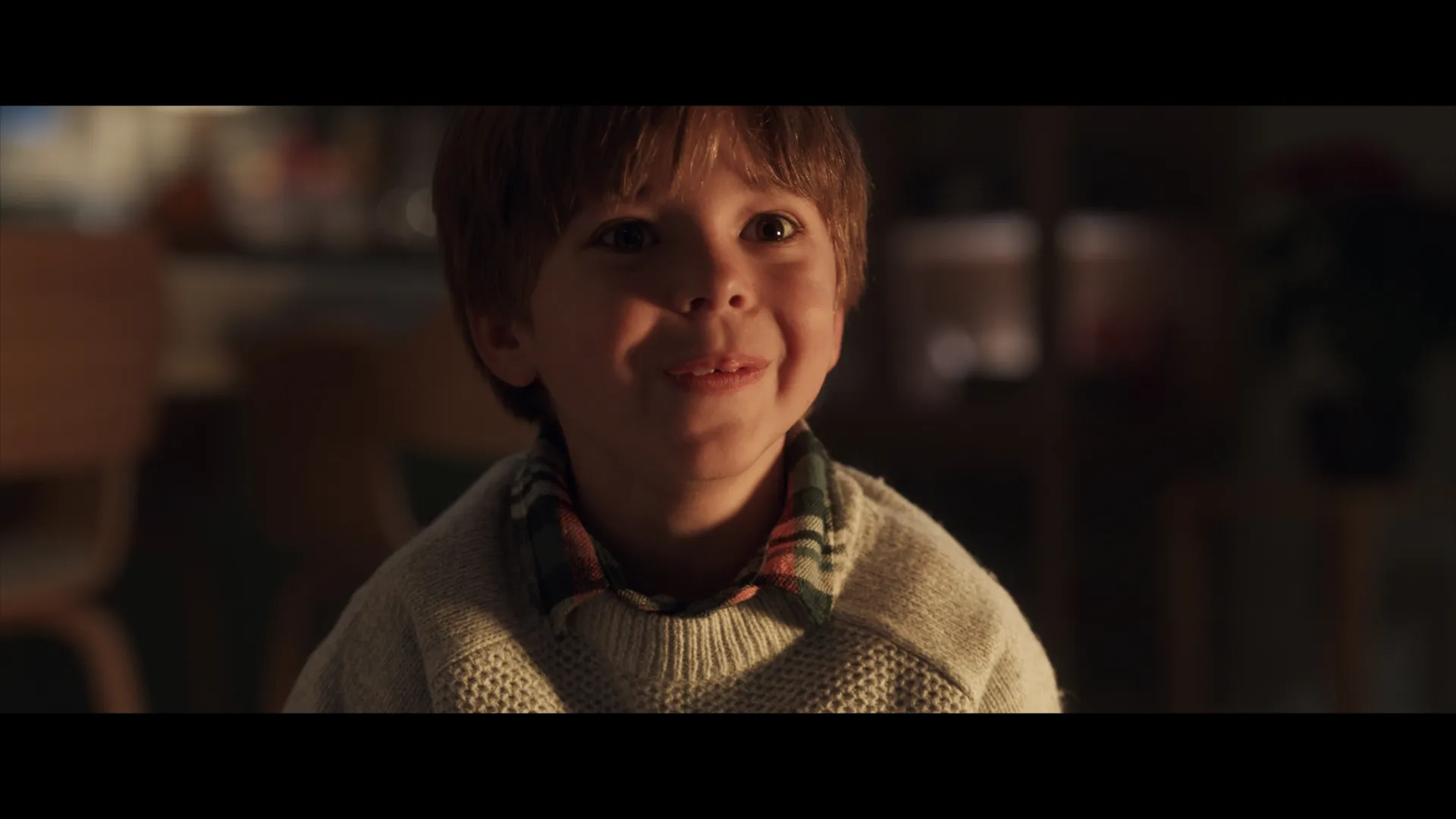 A young boy smiles brightly in warm Christmas light, his face filled with joy and wonder.