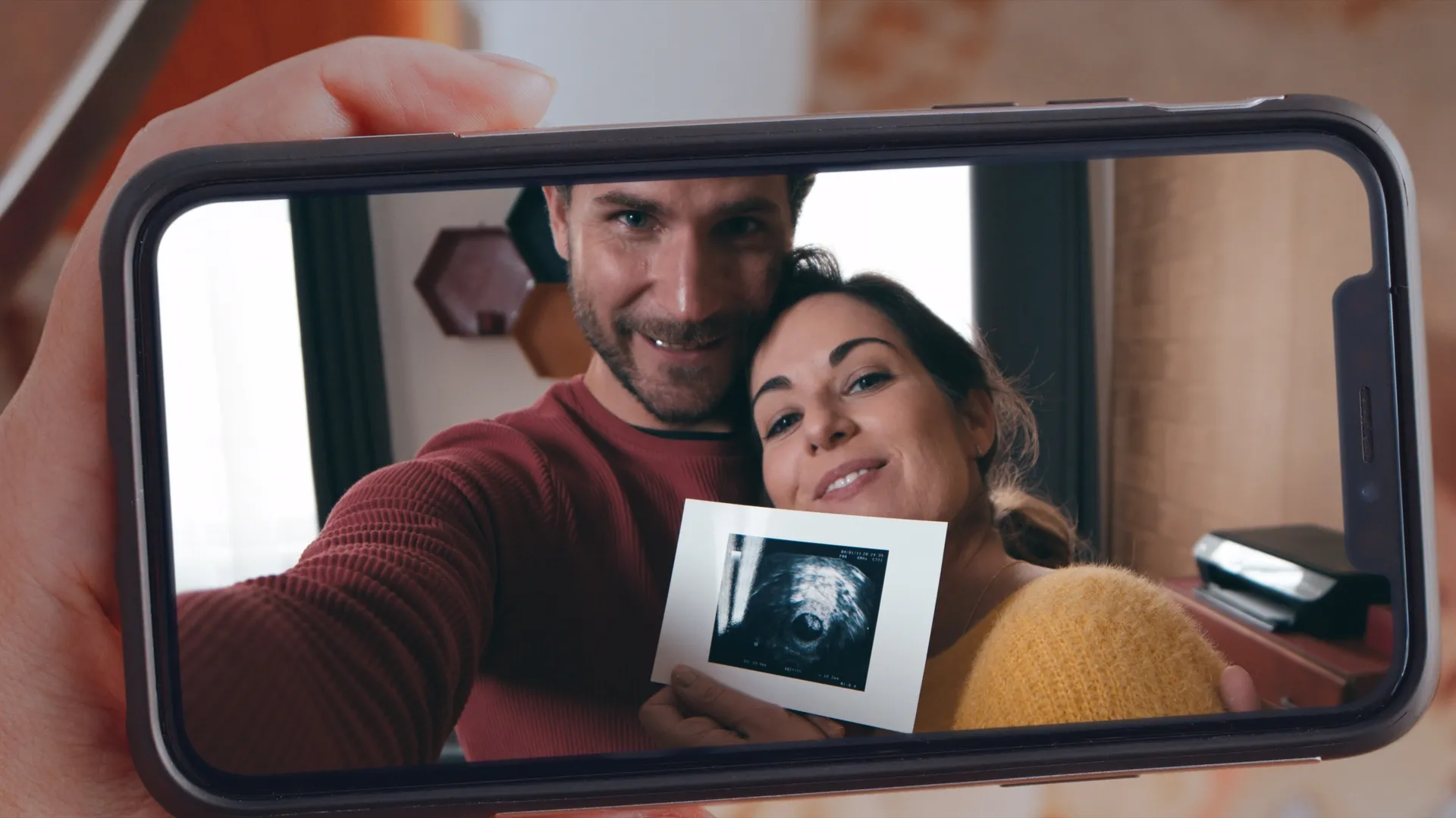 A phone screen showing a couple smiling and holding an ultrasound photo.