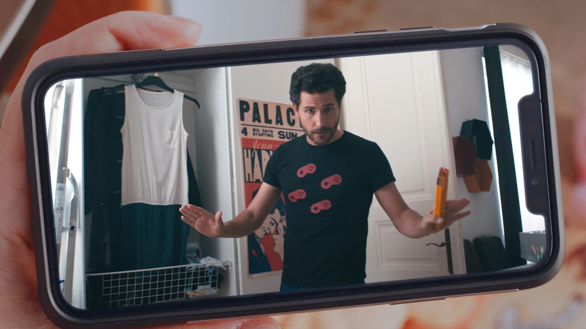 A phone screen showing a man standing in front of an open wardrobe, gesturing with his hands.