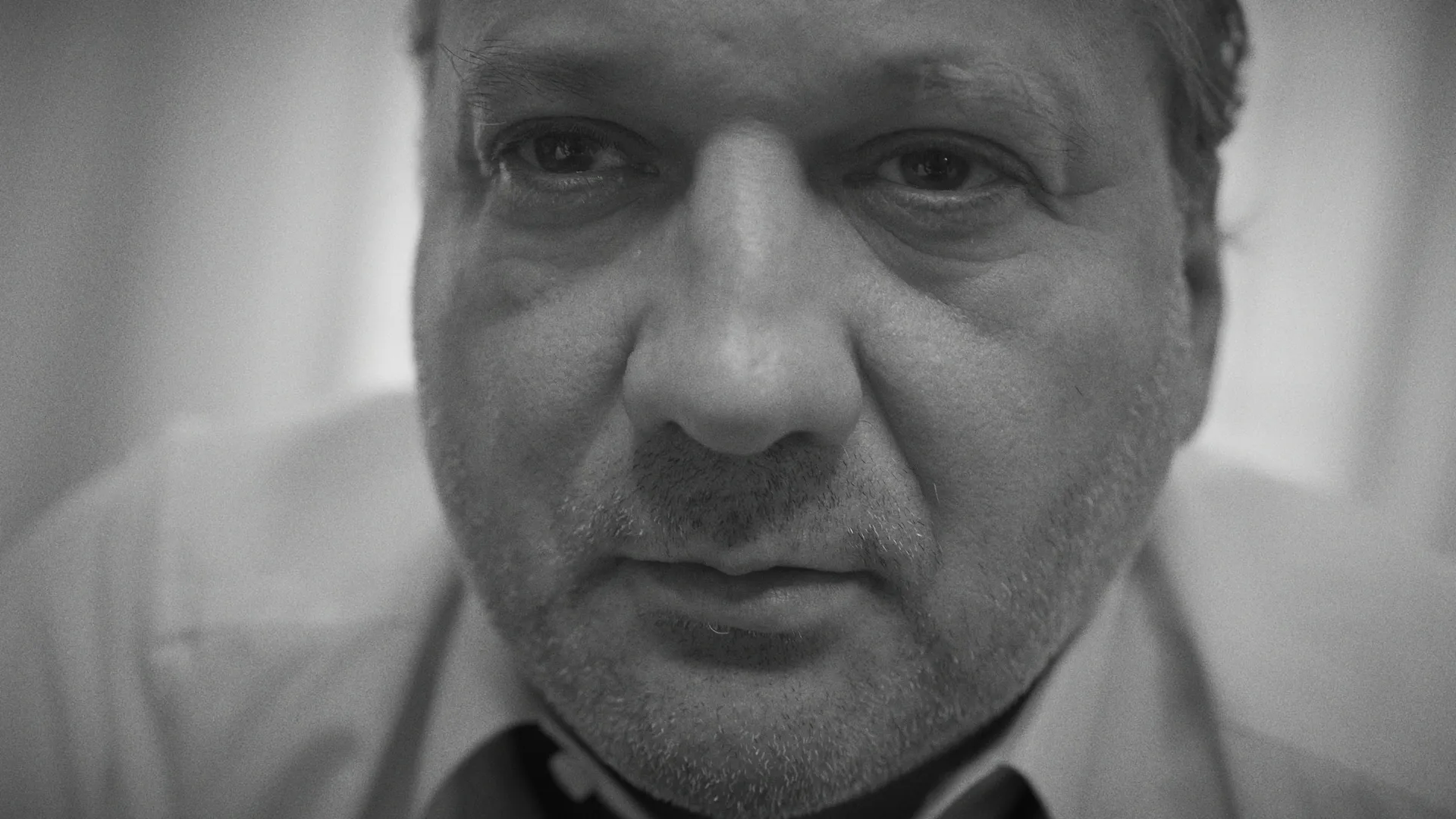 Close-up black-and-white portrait of a middle-aged man with a serious, tired expression.