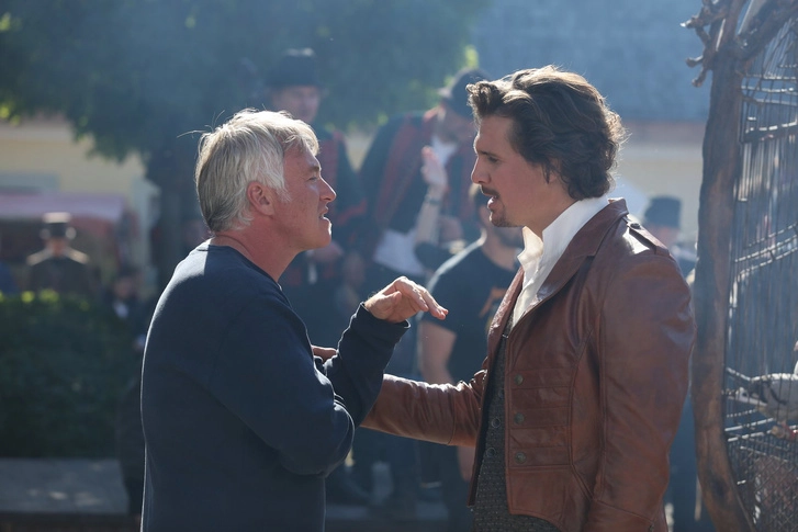 Two men standing outdoors engaged in a serious conversation in bright sunlight, with flash lighting enhancing the scene’s sharpness.