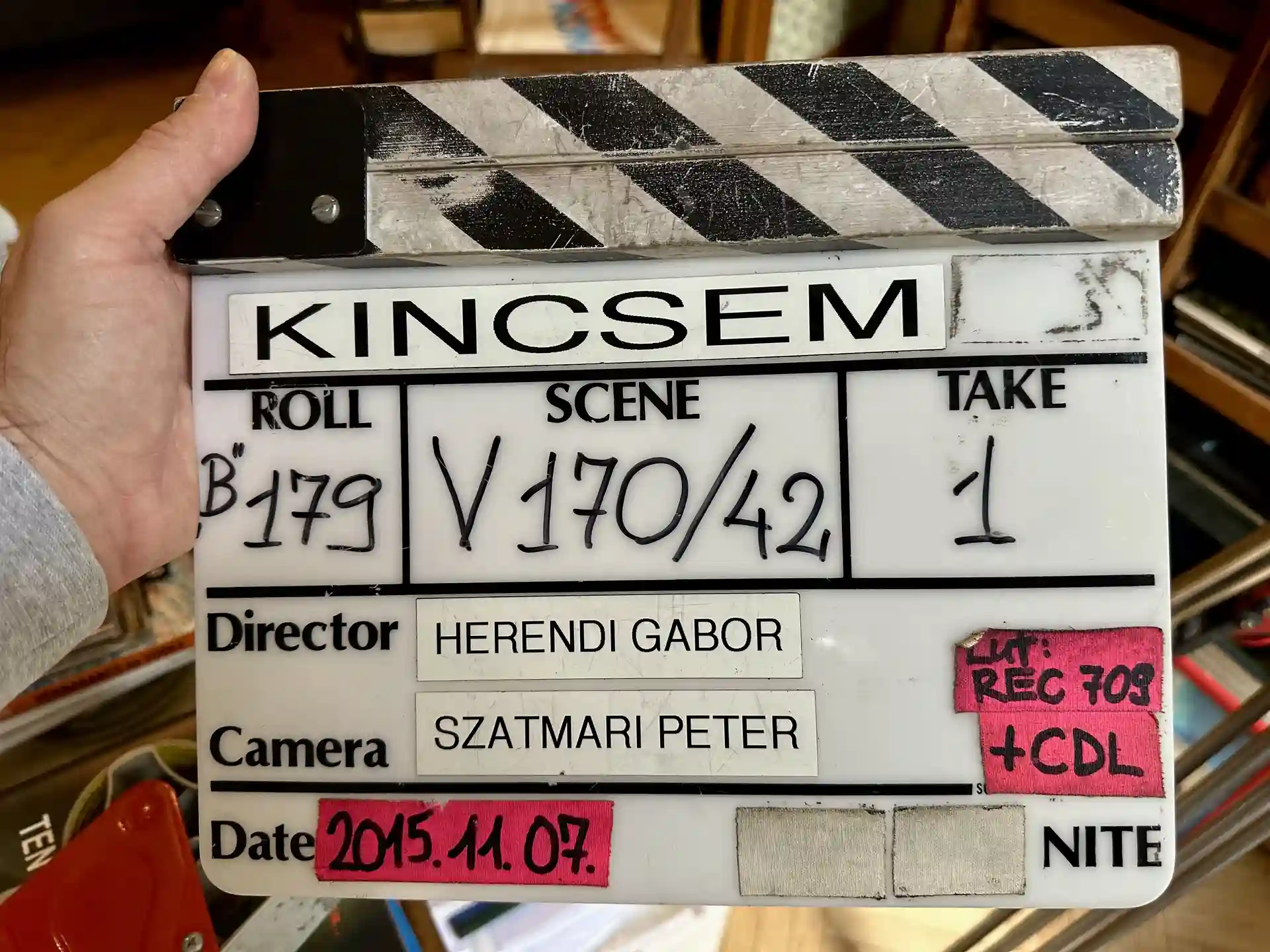 Close-up of a Kincsem film slate showing scene and take details, with handwritten notes and bright flash lighting emphasizing the clapperboard surface.