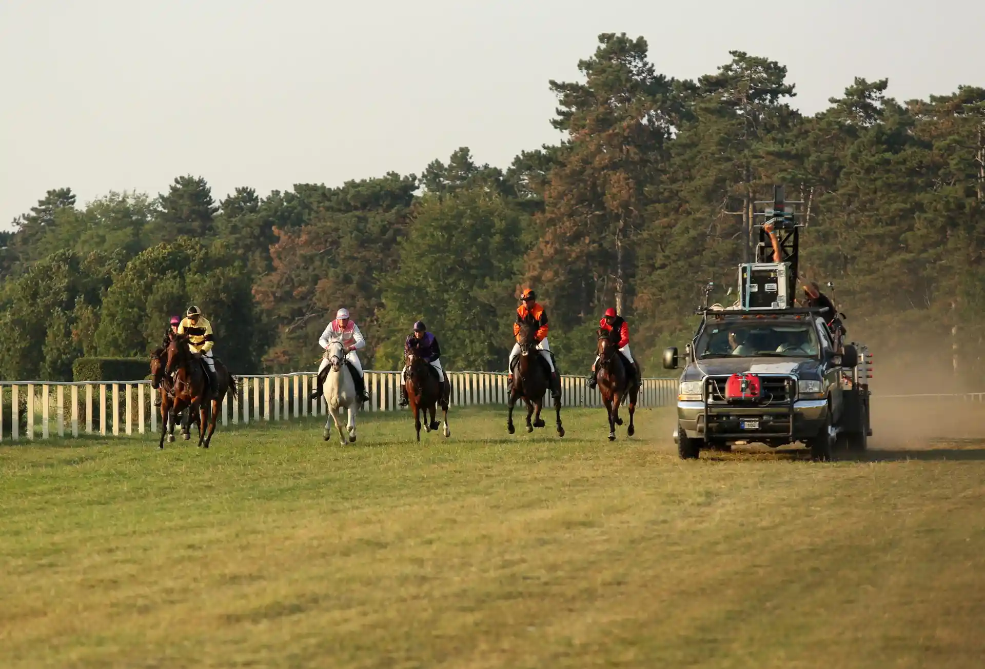 Horse riders racing across a grassy field alongside a camera rig vehicle filming the action, captured with strong flash lighting for clarity.