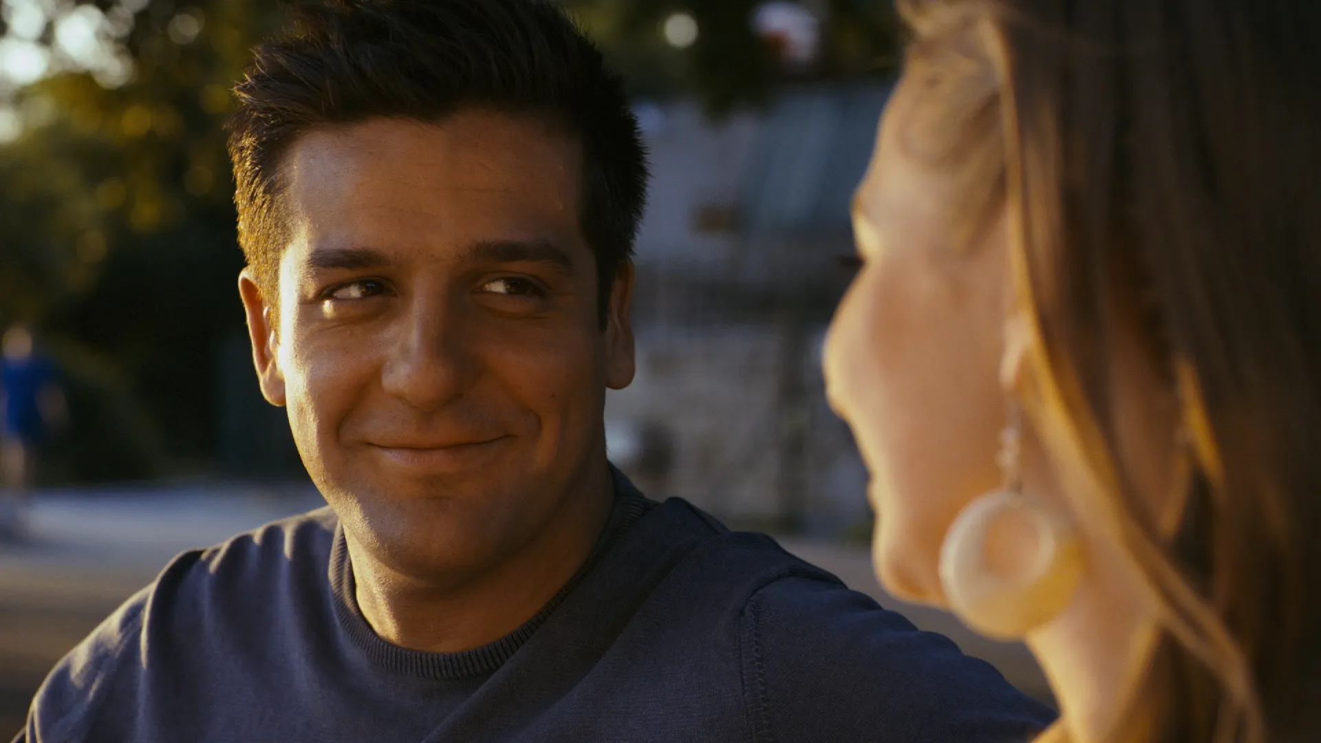 Man smiling warmly at a woman during an outdoor conversation at sunset.