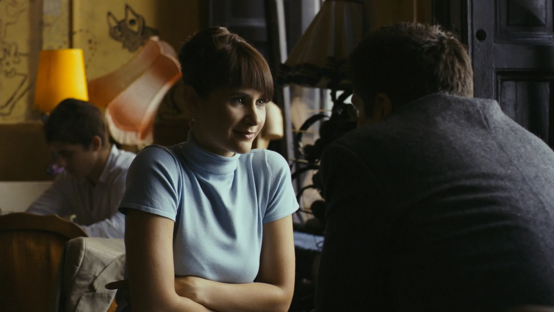 Woman sitting with folded arms, listening to a man in a dim, cozy room.