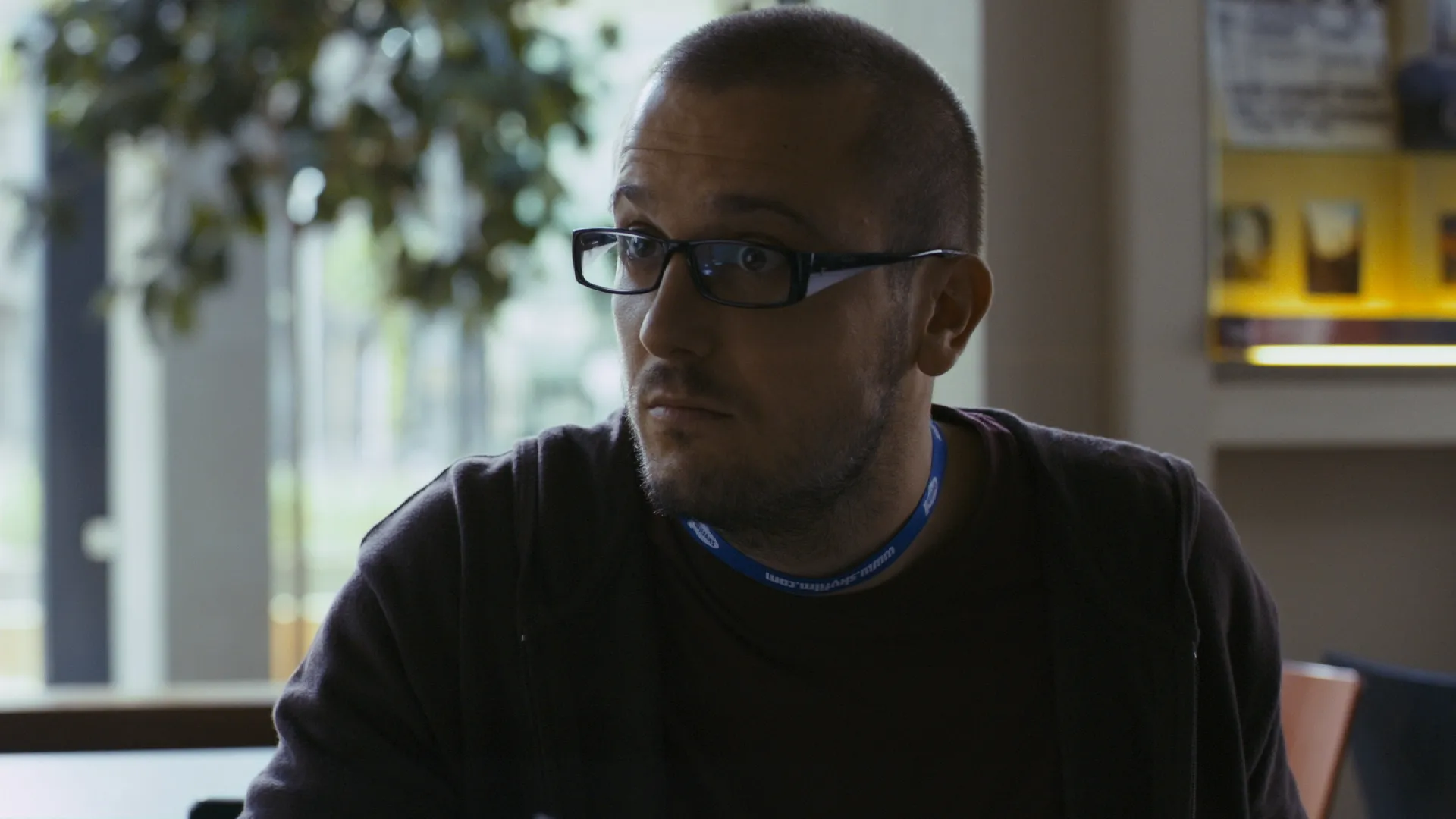 Man with glasses sitting indoors, looking to the side in soft, natural light.