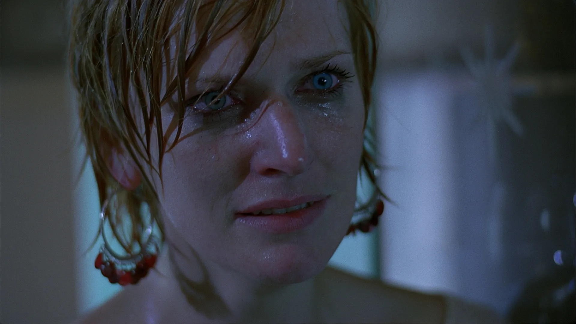 A woman with wet hair stands in blue-toned light, her expression tense and emotional as water droplets cling to her face.
