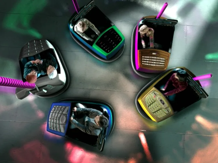 Three men sitting at a pub table raise tall glasses of beer in a cheerful toast, with other patrons chatting in the background.