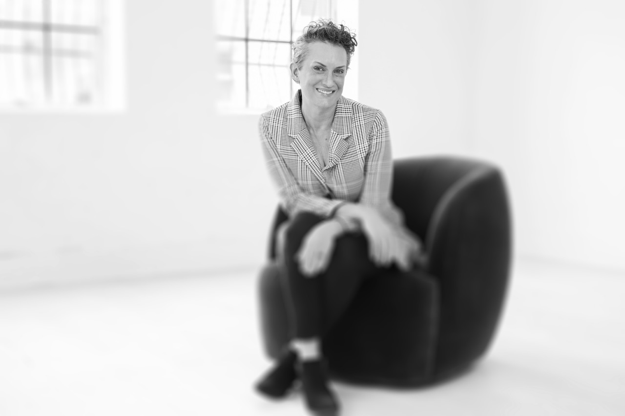 Black and white photo of Tessa siting on a black chair and smiling