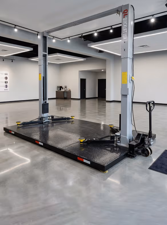 Portable car hoist with black diamond plate platform and two vertical gray posts in a showroom.