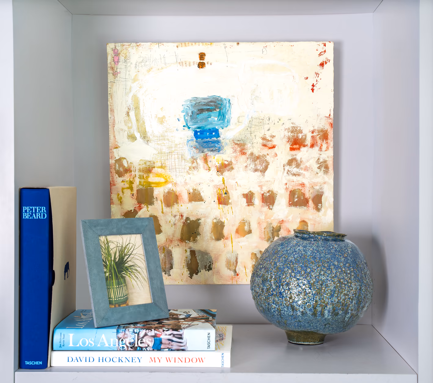 Abstract painting, blue glazed vase and art books displayed in a white shelf niche at Studio Home