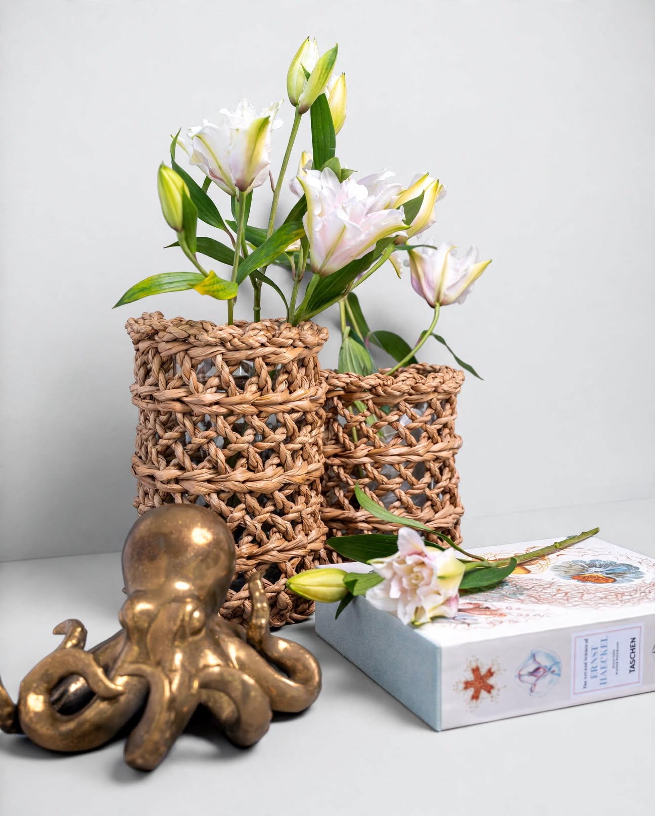 Woven vases with pink lilies beside a brass octopus sculpture and a decorative book