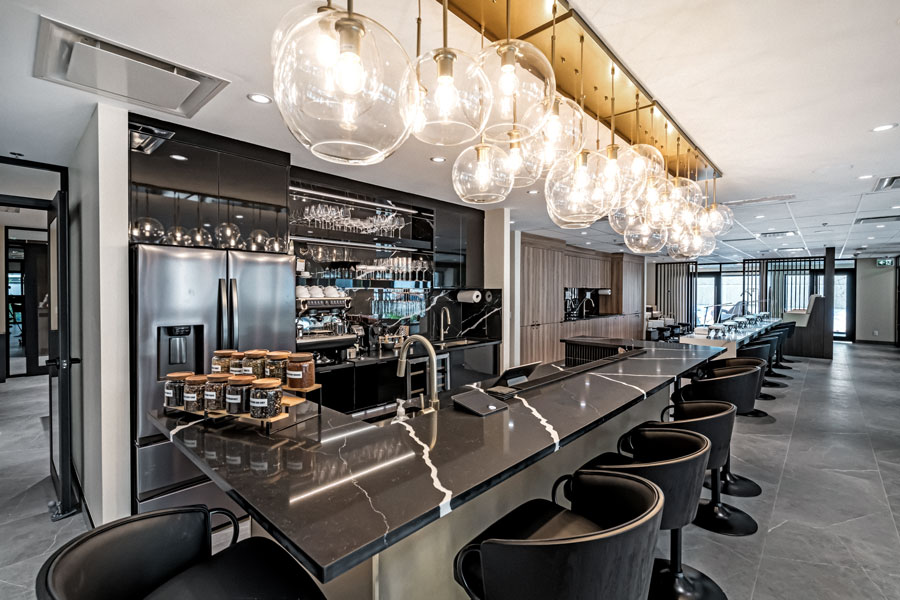 Modern spa café bar with marble counter, black stools, glass pendant lights, stainless appliances, and sleek contemporary interior.