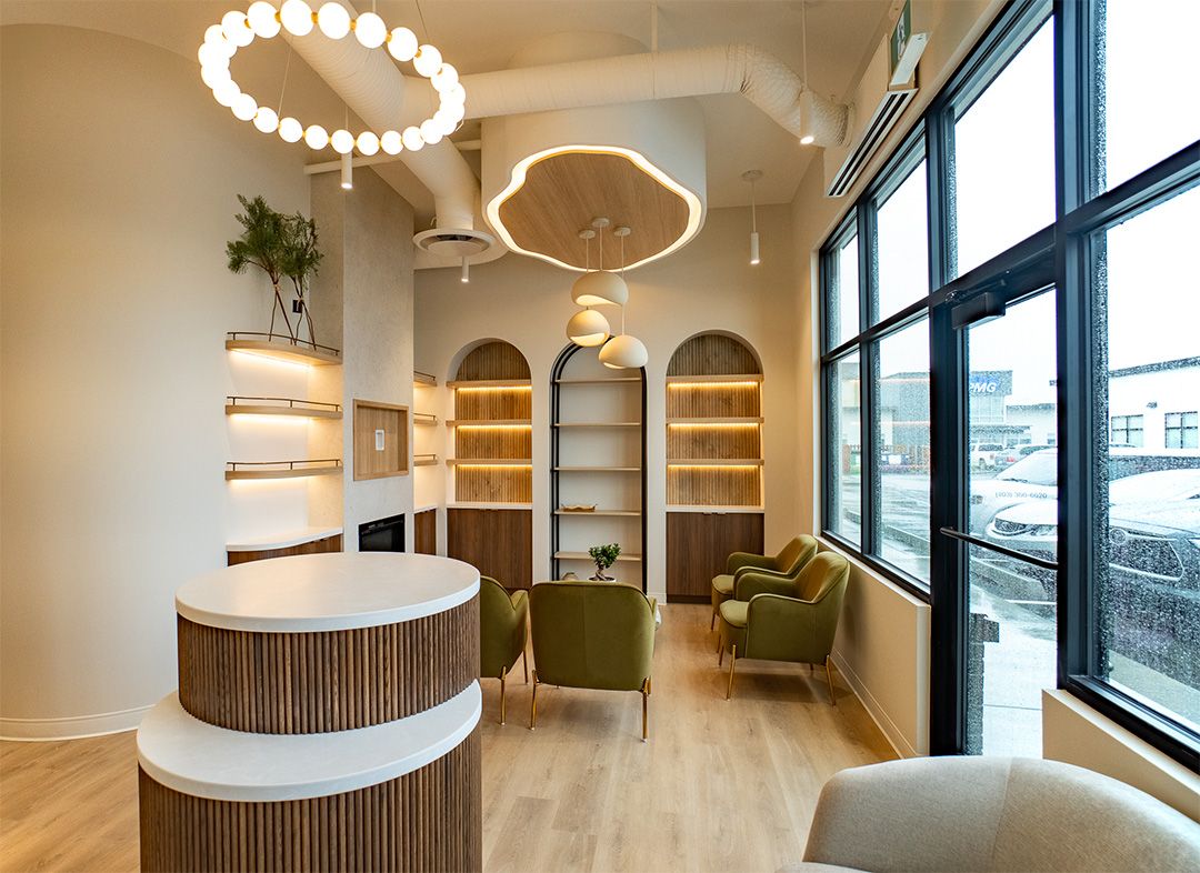 Calm waiting area with sage-green walls, soft seating, natural light, and warm wood flooring for a welcoming, spa-like feel.
