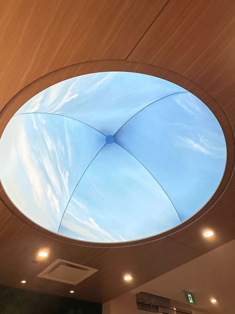Circular skylight in a wooden ceiling showing a partly cloudy blue sky.