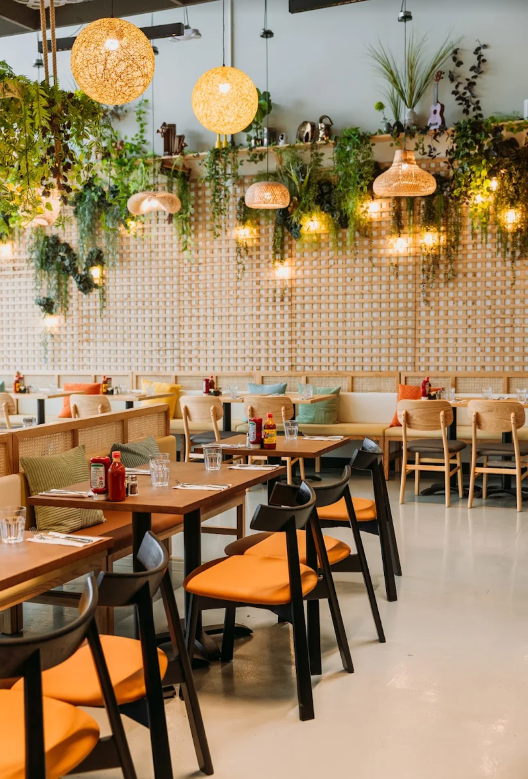 Bright, leafy bistro dining room with warm wood tables, woven pendants, and vibrant accent seating for a relaxed, inviting feel.