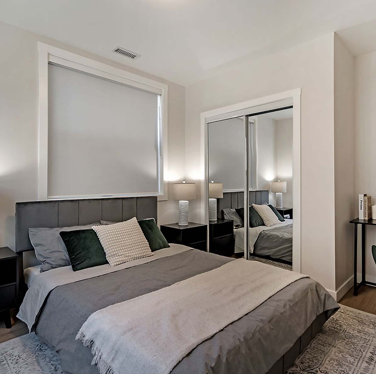 Calm modern bedroom with neutral layers, upholstered headboard, mirrored closet doors, and soft ambient lighting.