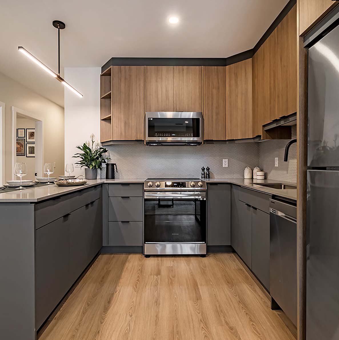 Contemporary U-shaped kitchen with warm wood uppers, matte grey lowers, stainless appliances, and minimalist linear lighting.