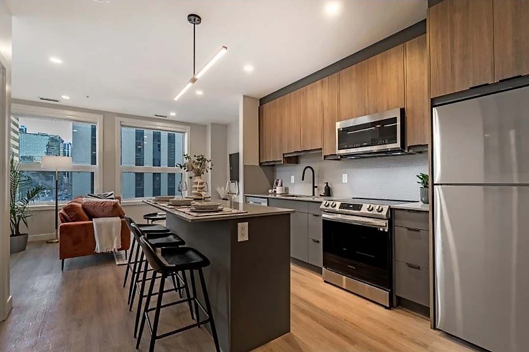 Open-concept kitchen with warm wood cabinets, grey island, pendant lighting, and city views flowing into the living area.