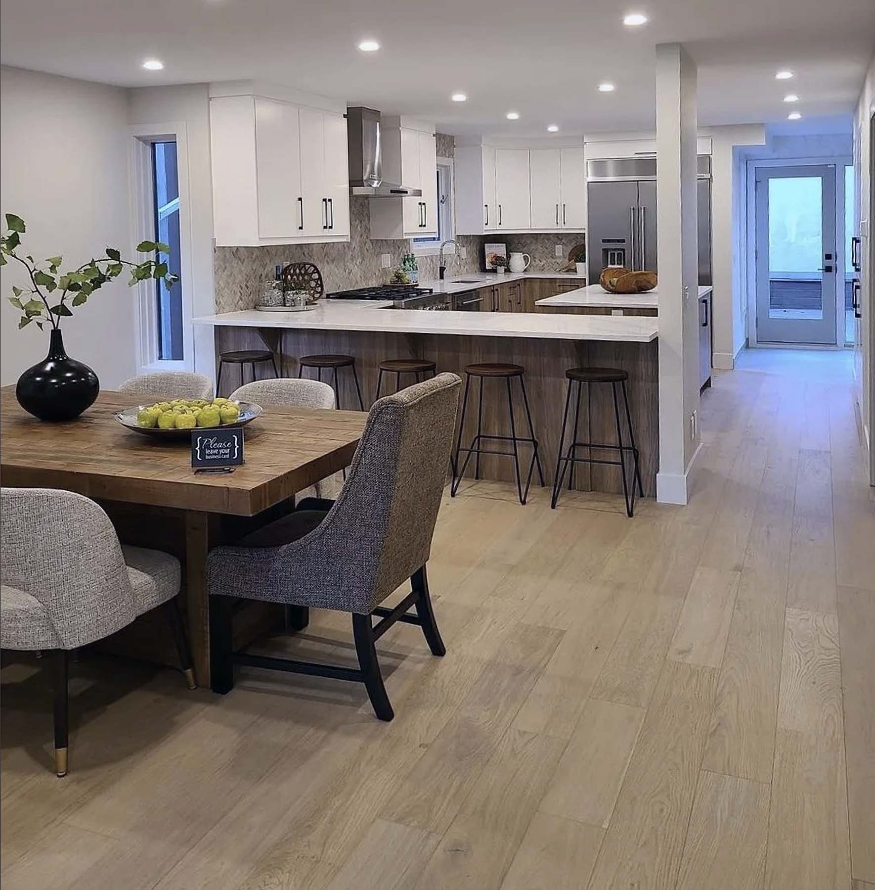Open-concept dining and kitchen with wood floors, large white island with bar stools, stainless appliances, and modern dining table.