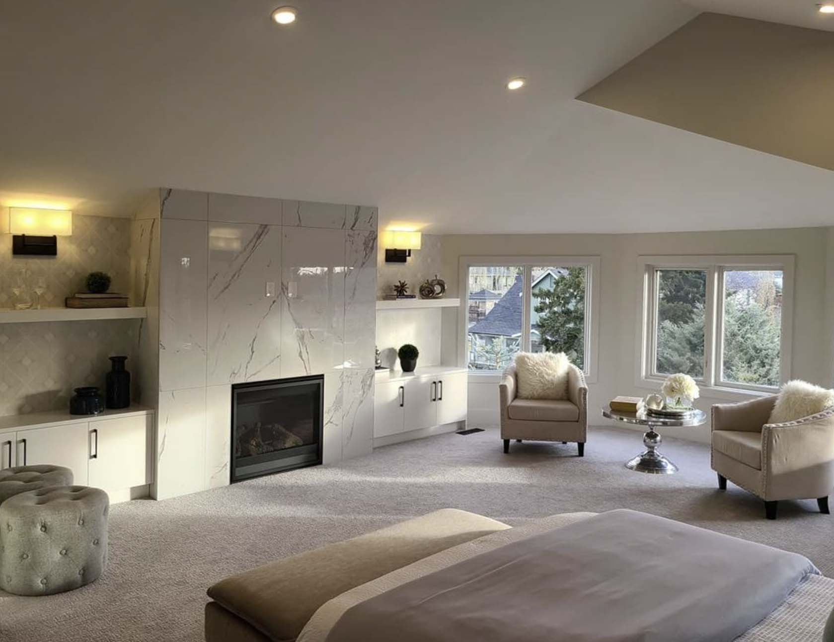 Spacious bedroom with marble fireplace, built-in shelving, cozy seating area, soft carpet, and large windows with daylight.