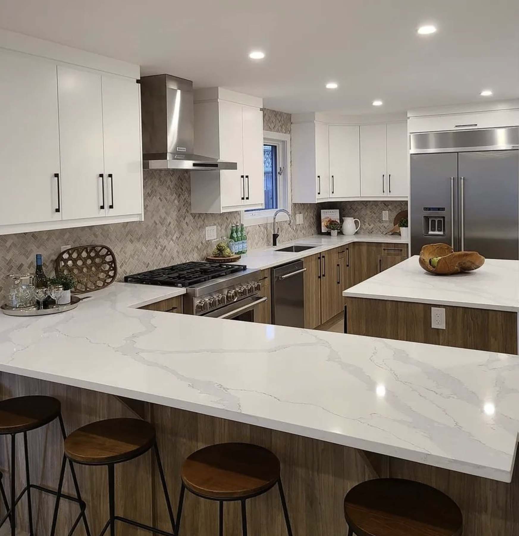 Modern kitchen with white quartz island, wood and white cabinetry, stainless appliances, herringbone backsplash, and bar stools.