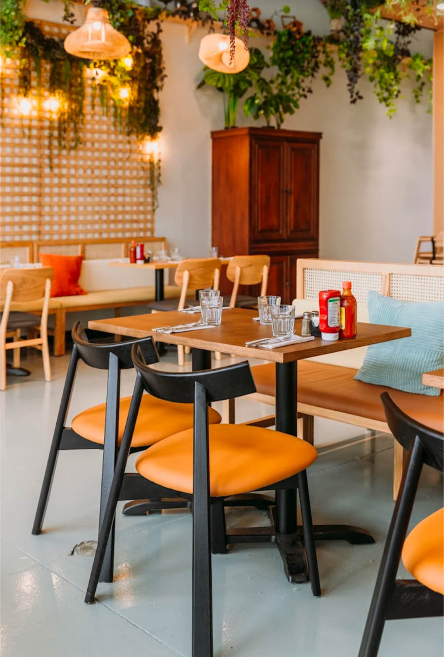 Warm wood tables, orange leather chairs, and lush hanging greenery create an inviting, cozy dining experience with soft ambient lighting.