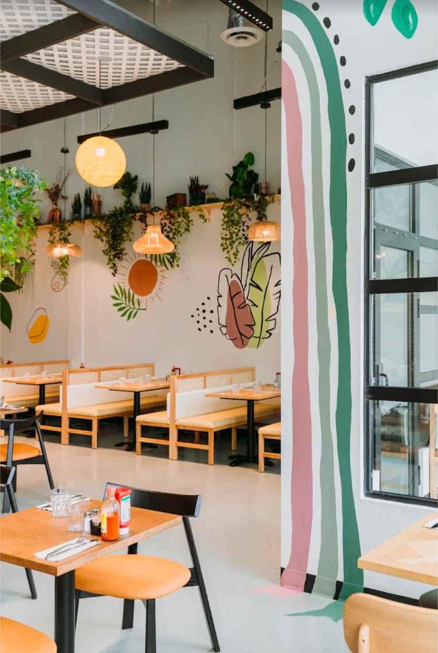 Playful wall mural, warm wood booths, and globe pendants blend with lush greenery for a bright, cheerful dining atmosphere.