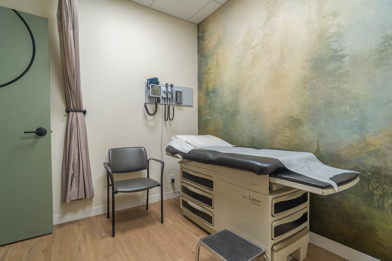 Calming exam room with nature mural, warm wood floors, modern medical equipment, and a soft privacy curtain.