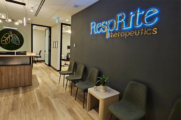 RespRite Therapeutics reception area with illuminated logo sign, wood desk, moss artwork, globe pendants, and grey waiting chairs.