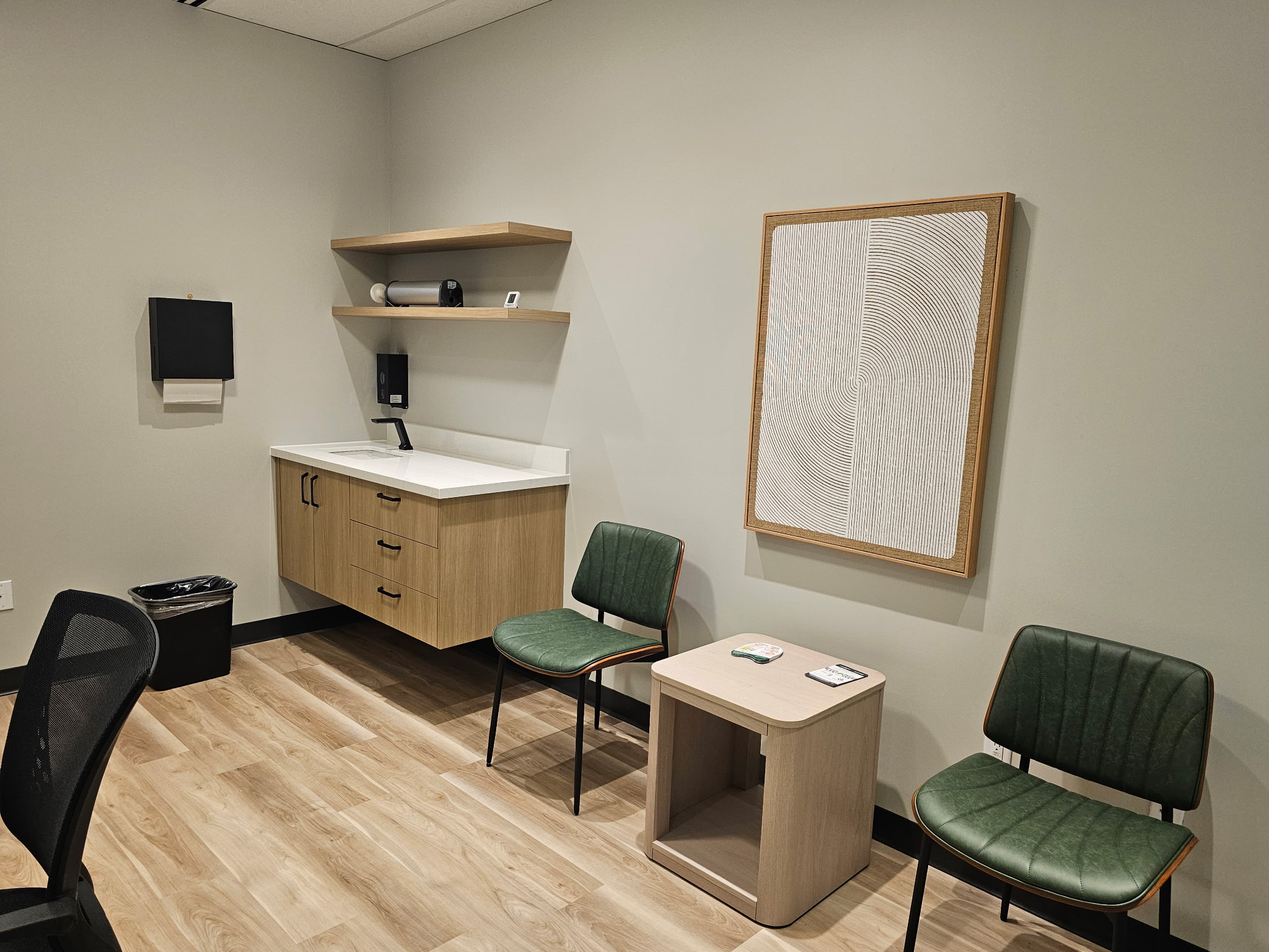Consulting room with floating wood vanity, green mid-century chairs, open shelving, and large abstract white line artwork.