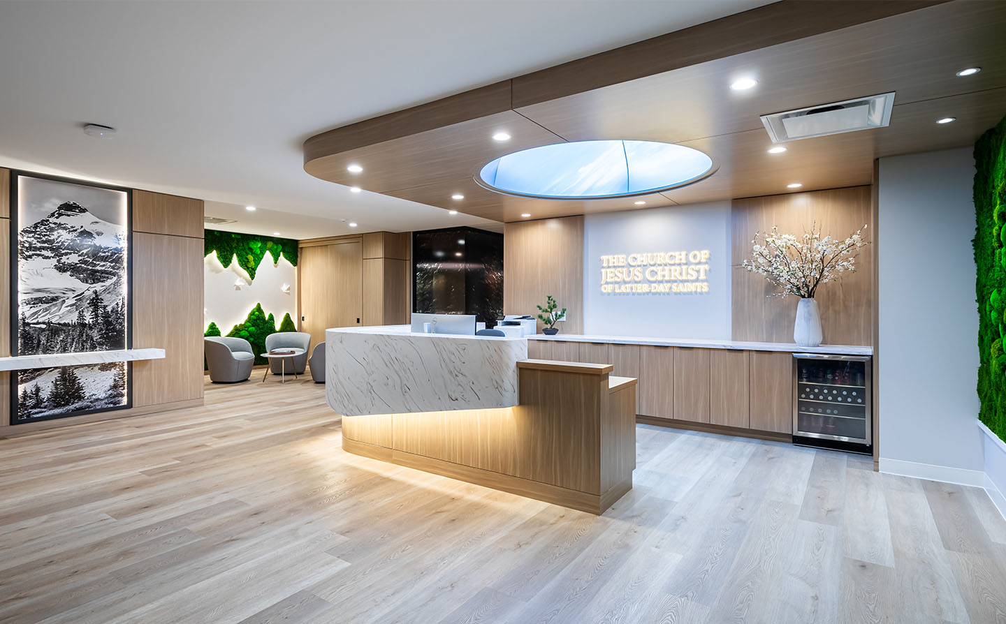 Modern reception area with marble desk, wood paneling, moss wall, and illuminated oval skylight above.