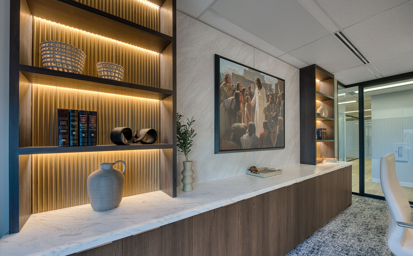 Built-in shelving with LED strip lighting, fluted wood backing, books, vases, and large religious painting.