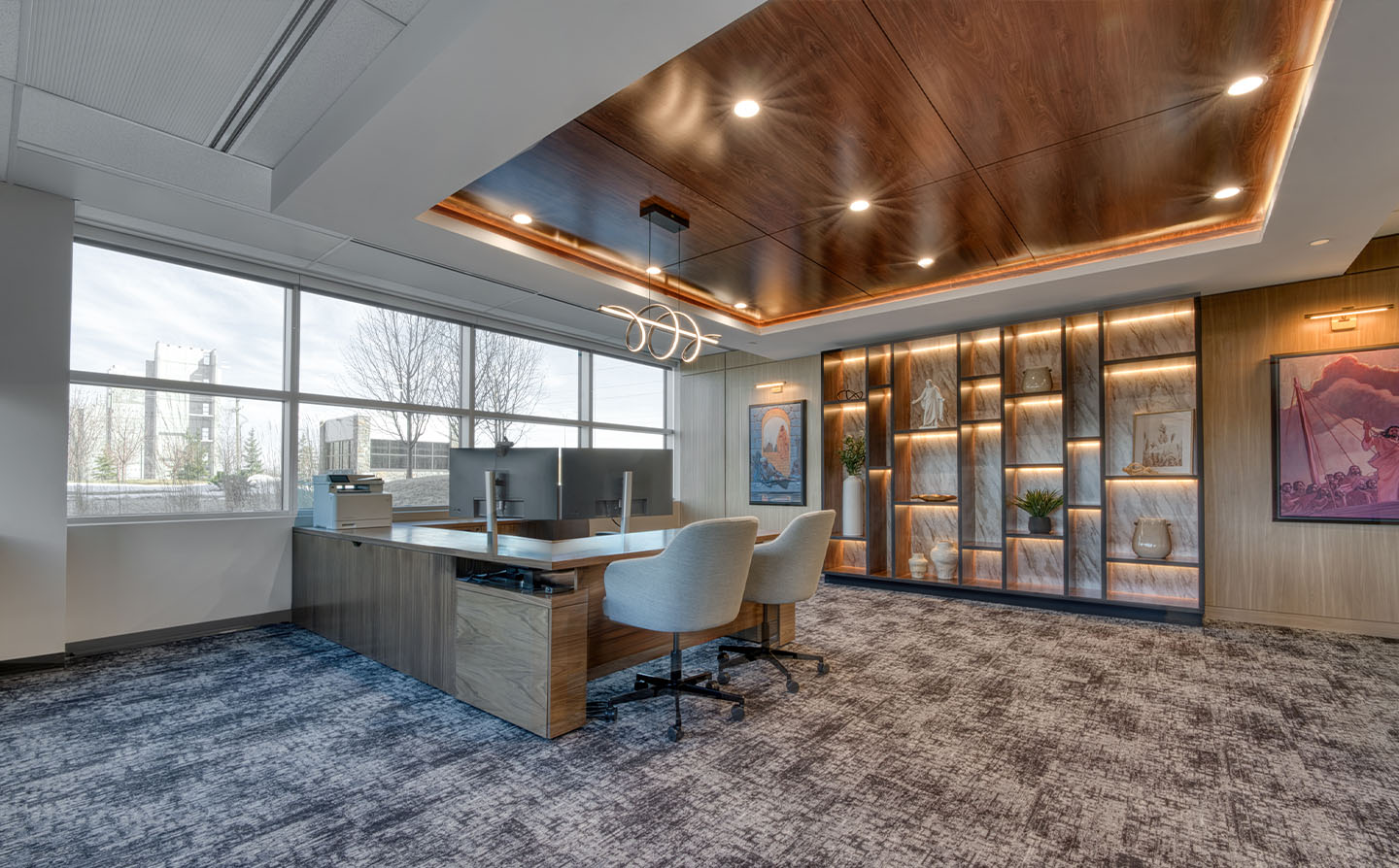 Spacious executive office with walnut tray ceiling, LED cove lighting, backlit display wall, and large windows.