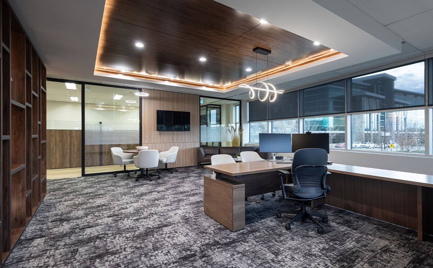 Executive office with dark walnut millwork, curved pendant light, glass walls, and city views through large windows.