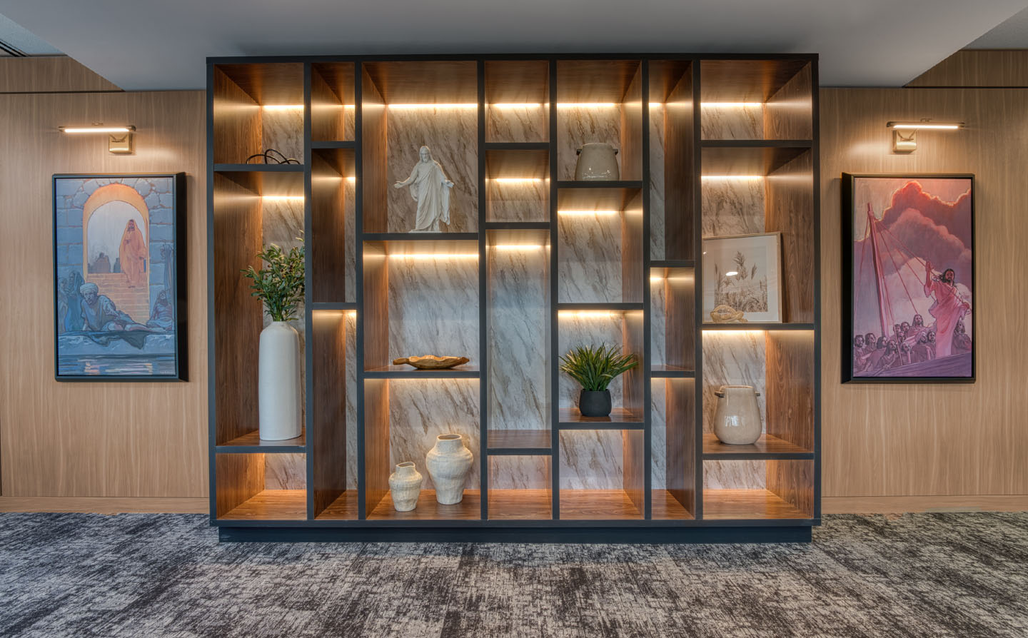 Floor-to-ceiling backlit display shelving with marble inlay, decorative objects, and flanking religious artwork.