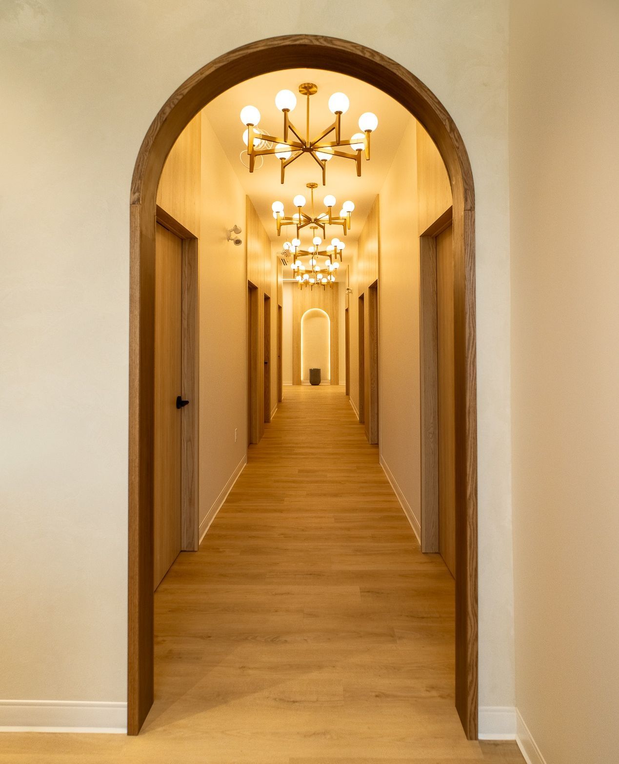 Warm hallway seen through wood-trimmed arch with brass sputnik chandeliers repeating into distance