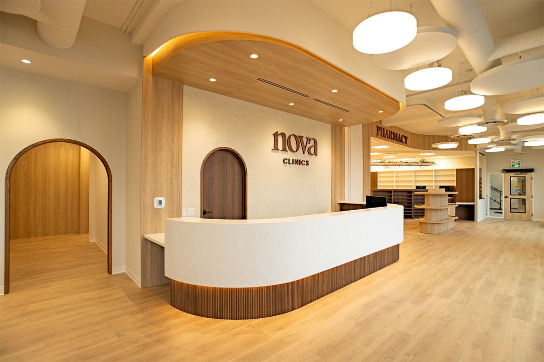 Nova Clinics curved reception desk with walnut fluting, arched doors, and pharmacy beyond