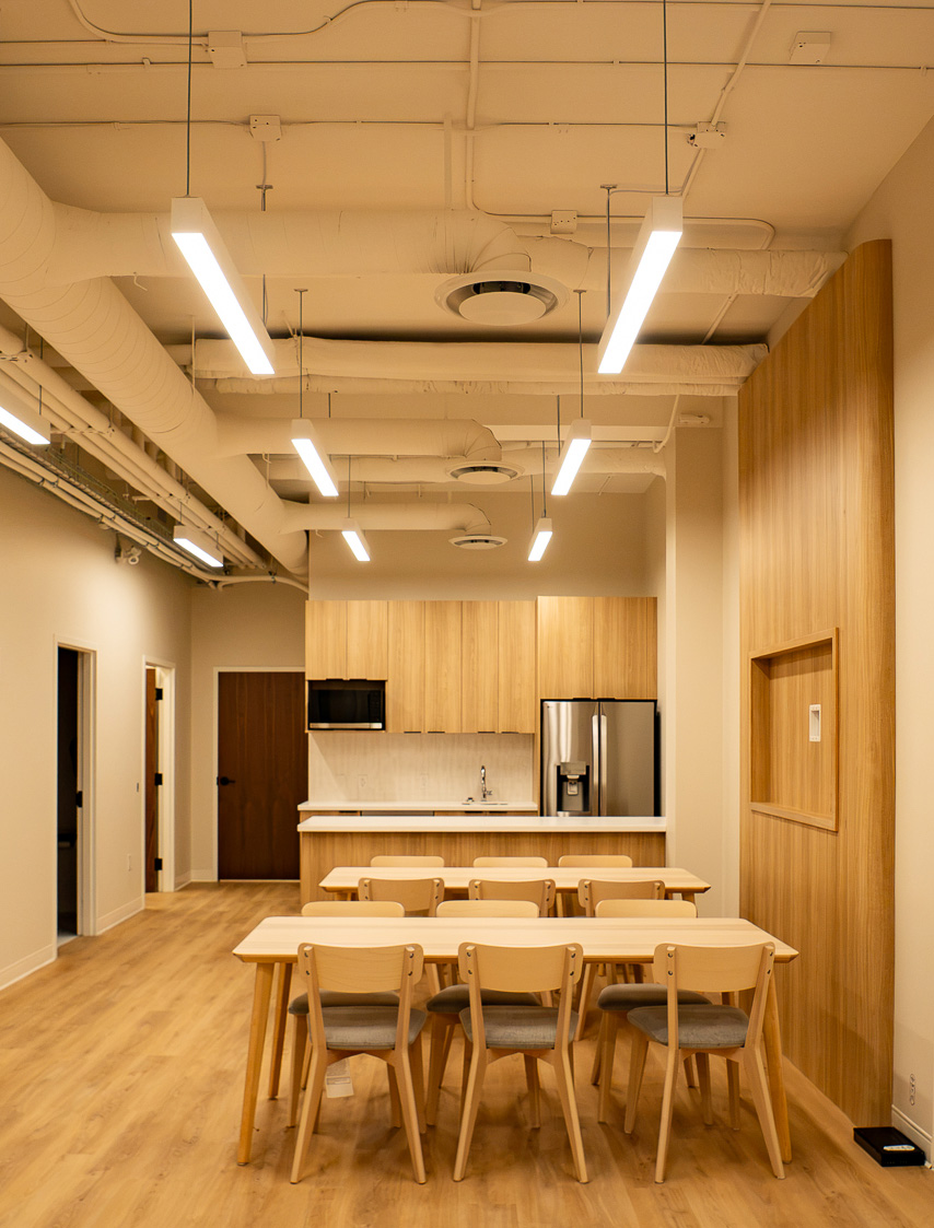 Staff break room with wood cabinetry, long dining table, and exposed ceiling