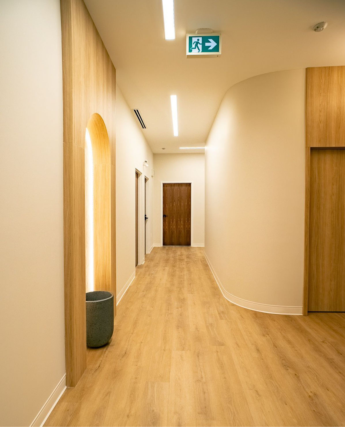 Clean clinic corridor with arched backlit niche, wood doors, and curved wall detail