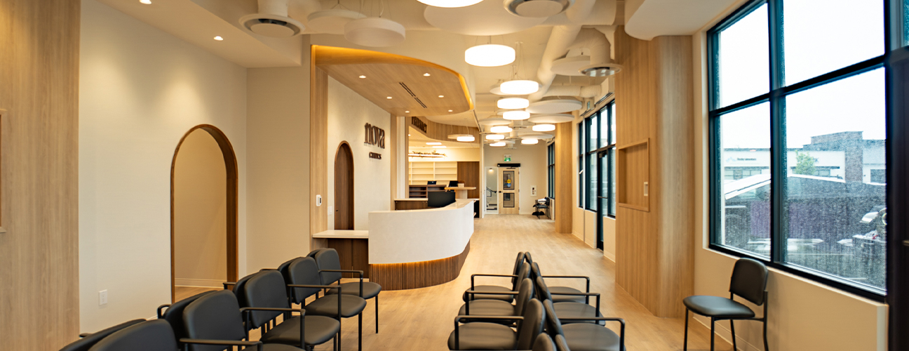 Bright clinic waiting area with black chairs, curved reception desk, wood accents, and large windows