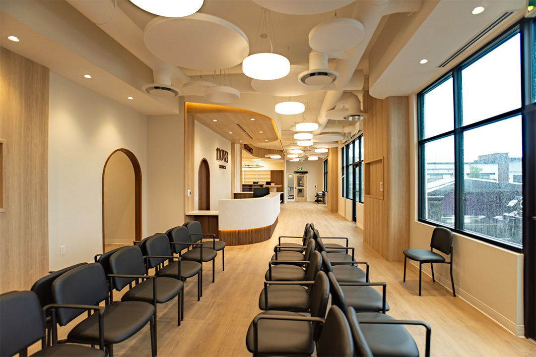 Bright clinic waiting area with black chairs, curved reception desk, wood accents, and large windows