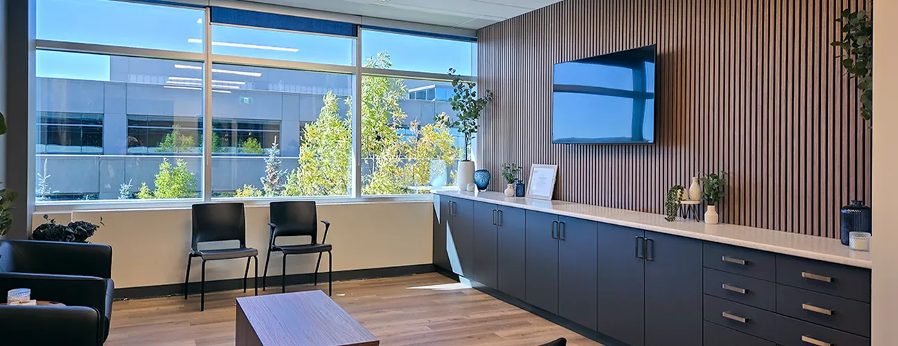 Bright clinic waiting area with black chairs, curved reception desk, wood accents, and large windows